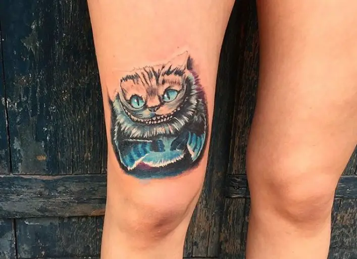 Cheshire Cat with blue eyes and blue lower body tattoo above the knee