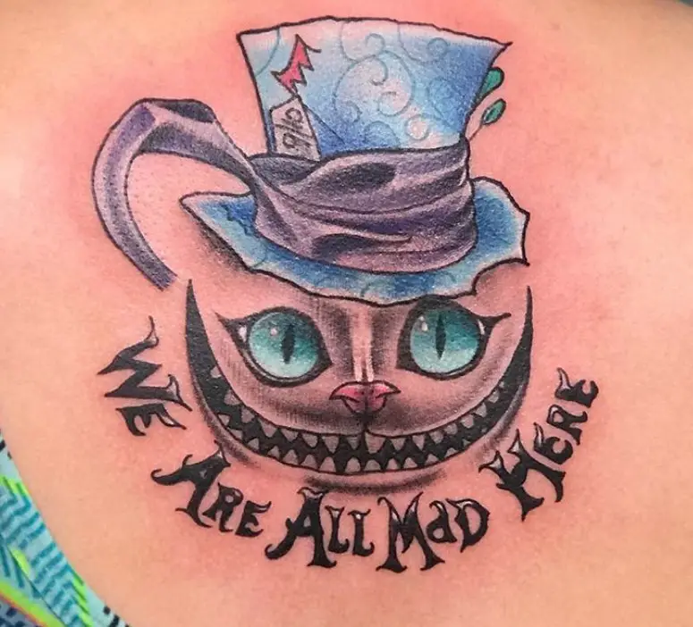 black and gray Cheshire Cat with pink nose and aqua blue eyes wearing a blue hat wrapped with purple blue fabric with words 