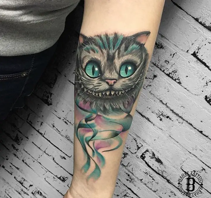 black and gray Cheshire Cat with green eyes with lines of green color on its fur tattoo on the forearm