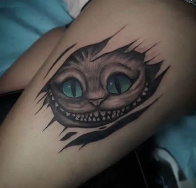 simple black and gray face of Cheshire Cat with blue green eyes tattoo on the leg