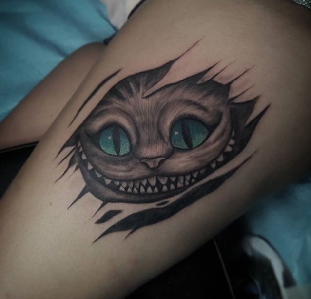 simple black and gray face of Cheshire Cat with blue green eyes tattoo on the leg