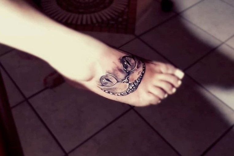 simple black and gray Cheshire Cat tattoo on the feet
