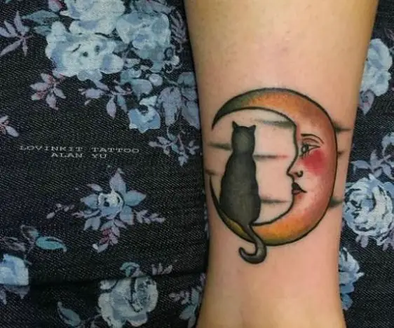 a black cat sitting in the crescent moon tattoo on the leg