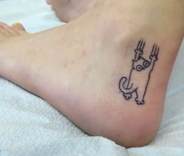 a falling outline of a cat tattoo on the ankle