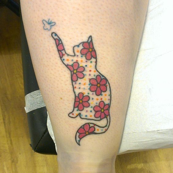 outline of a cat with flowers and colorful dots tattoo on the thigh