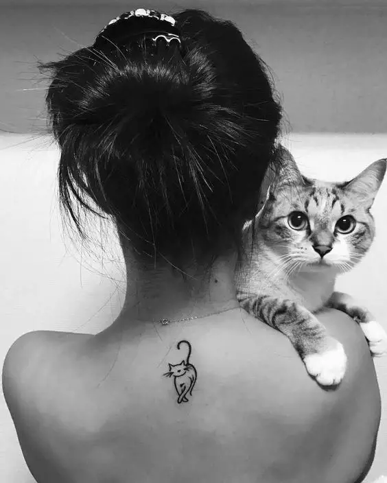 a woman with a sleek outline of a cat tattoo on the back while carrying her cat