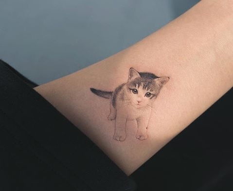 a minimalist black and white kitten tattoo on the wrist