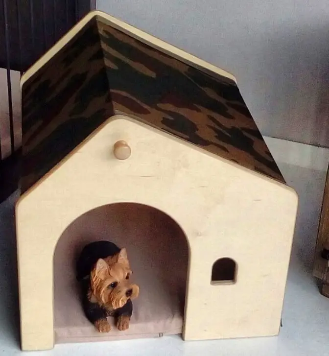 A modern dog house with a camouflage on the roof and a small dog lying inside
