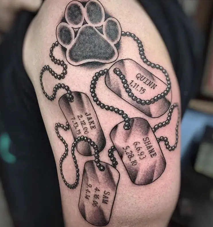 necklace with stainless pendants with name and dates of dogs connected to a paw print tattoo on shoulder