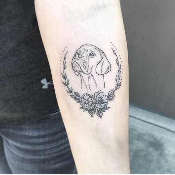 outline of dog's face around flowers and leaves tattoo on forearm