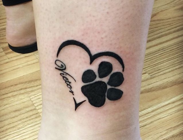 black paw print in heart shape with a name tatoo on the leg