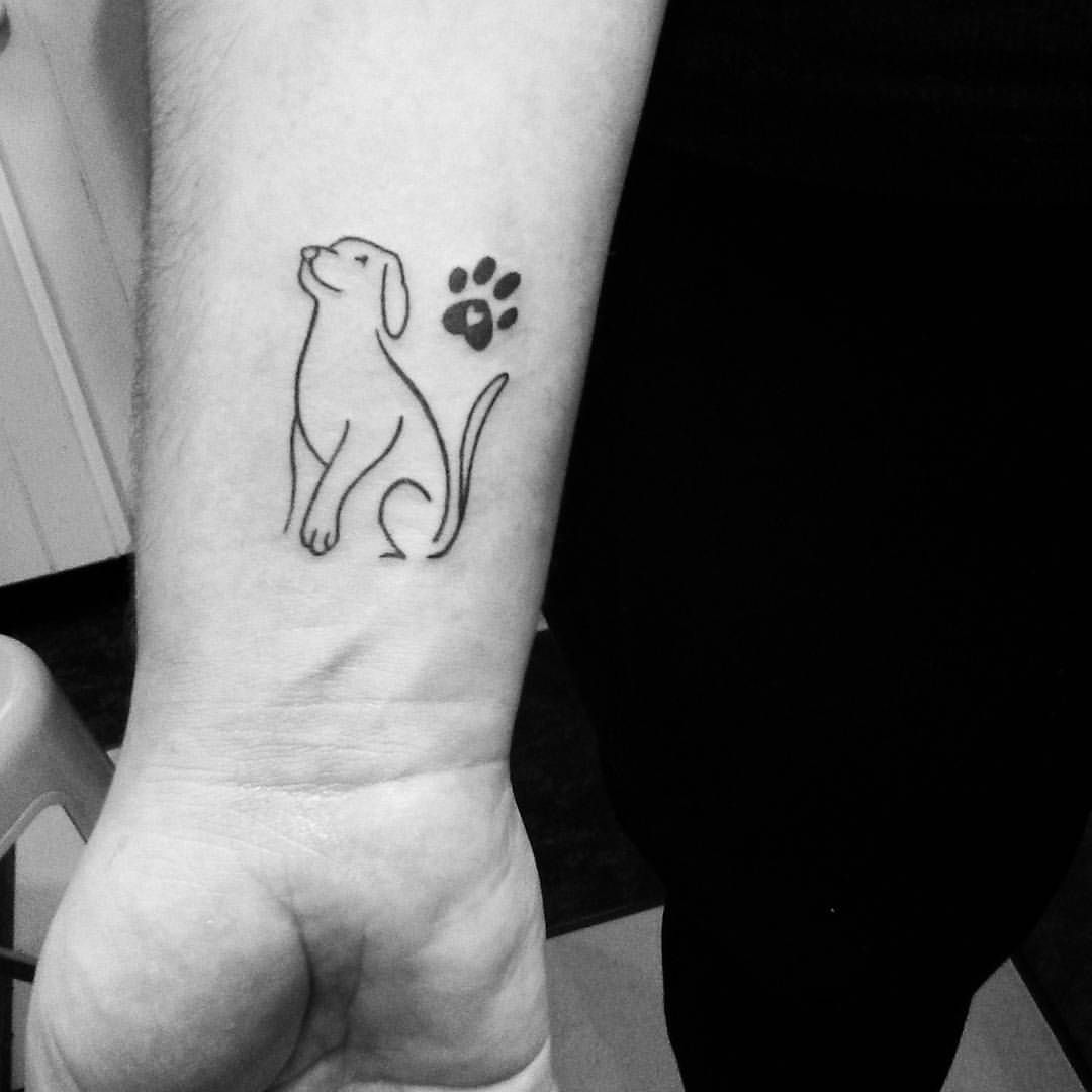 outline of a sitting dog wile looking up with a paw print next to him tattoo on the wrist