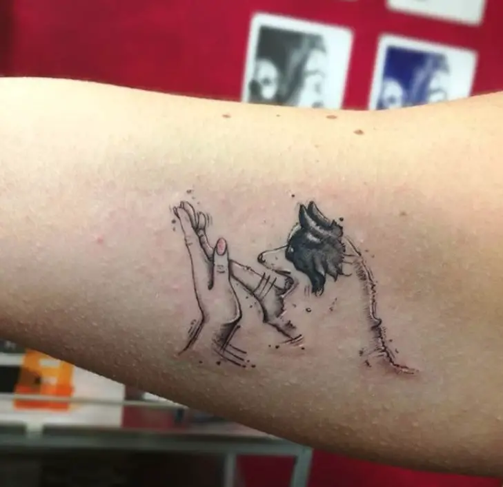 Black and gray outline of a Border Collie giving a paw to the hand tattoo on the biceps