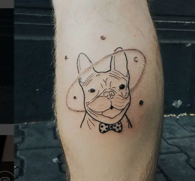 outline smiling face of a French Bulldog wearing a pulka dotted bow tie and a galaxy ring around its head with stars and moon around him tattoo on the leg