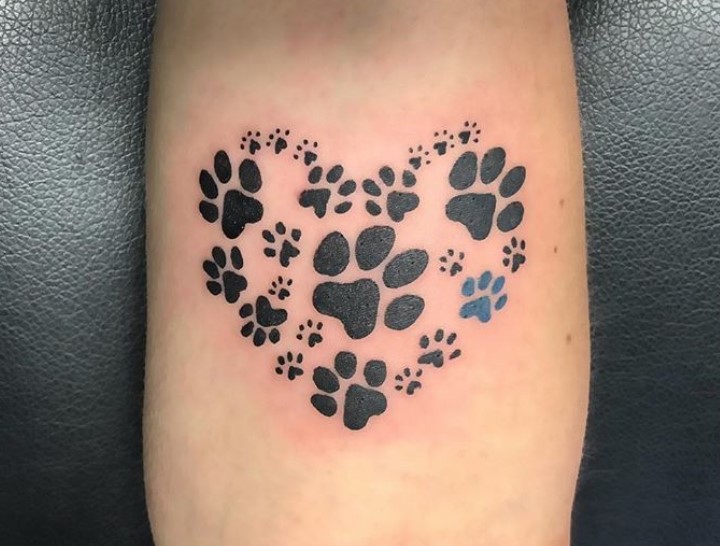 large and small paw prints in heart shape tattoo on forearm