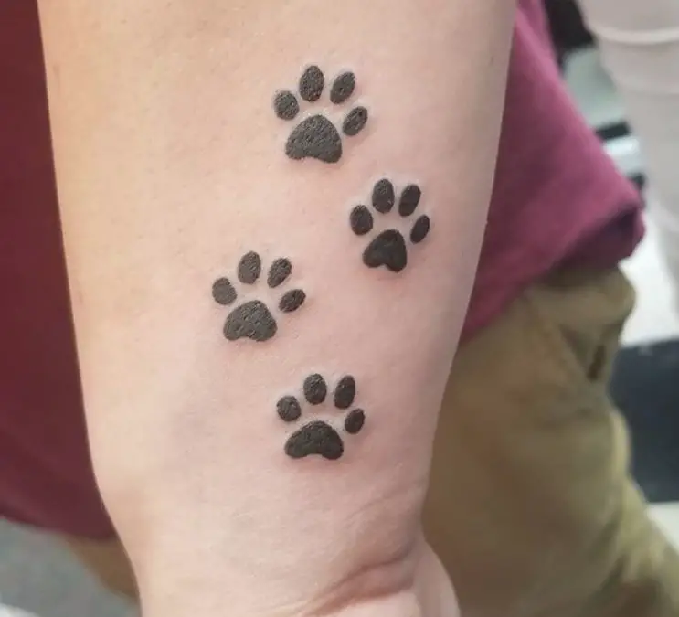 four small paw print tattoo on the side of the wrist