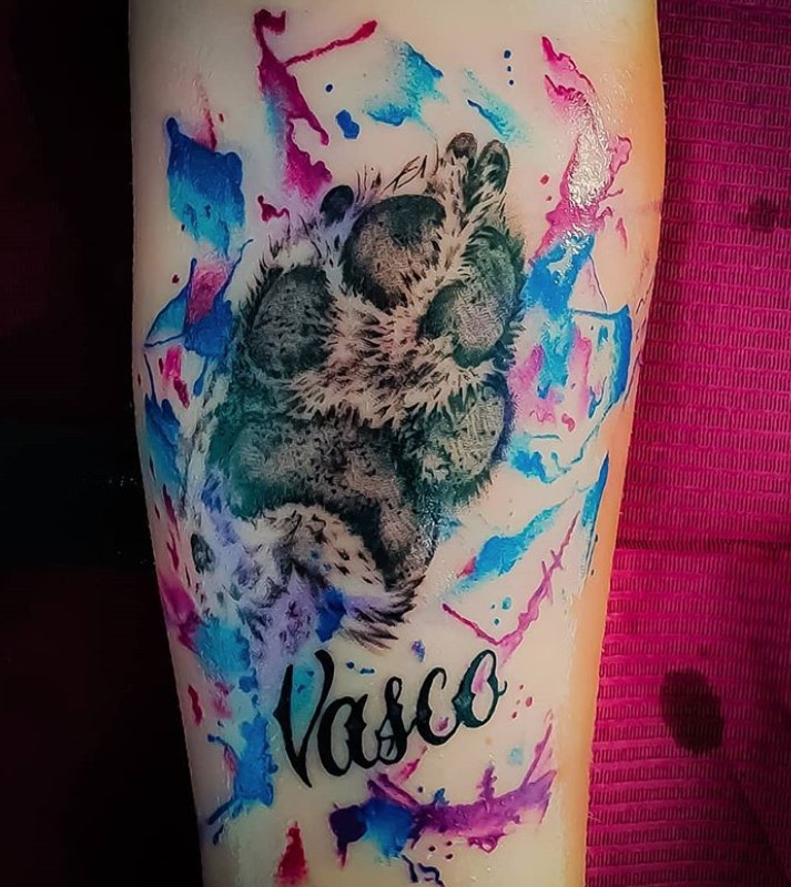 black paw print tattoo win splash of blue and pink paint tattoo on forearm