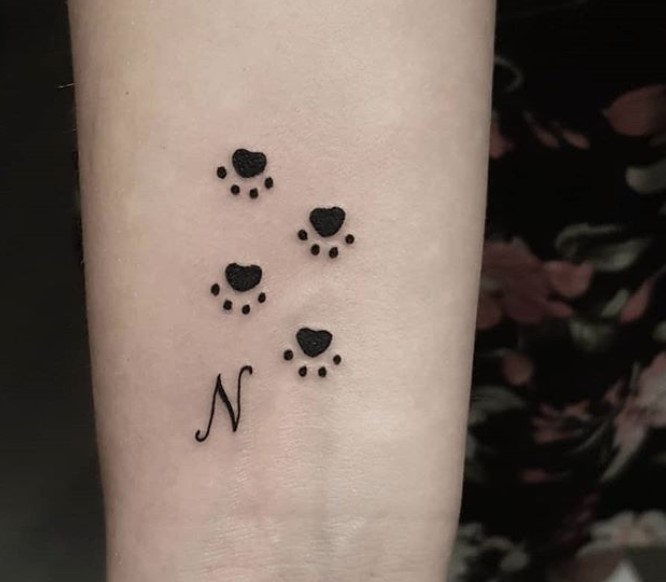 four paw prints with Italic initial tattoo on wrist