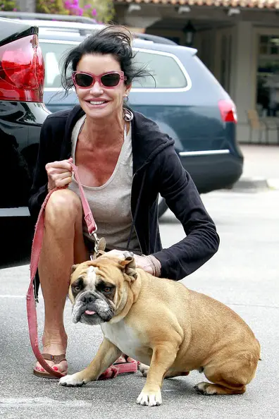 Janice Dickinson on the pavement petting her English Bulldog