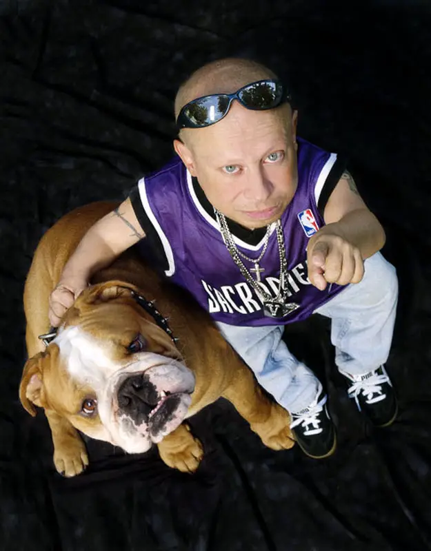 Verne Troyer sitting on the floor while pointing its finger with his English Bulldog sitting beside him