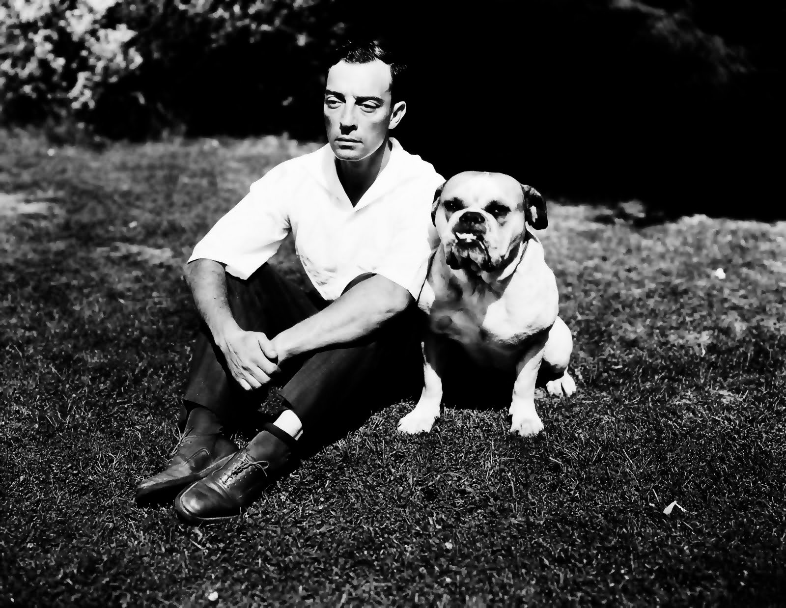 black and white photo of Buster Keaton sitting in the garden with his English Bulldog sitting beside him