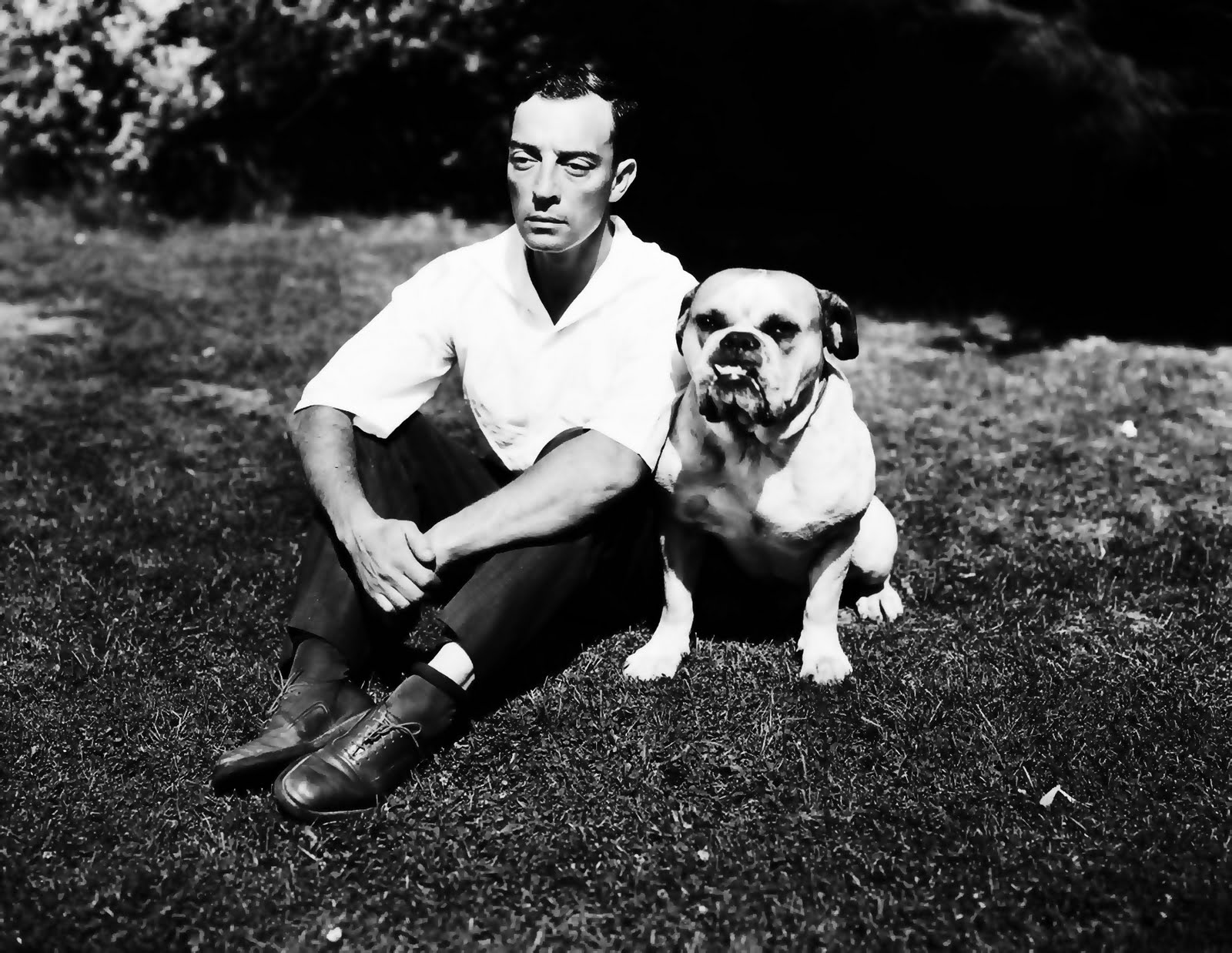 black and white photo of Buster Keaton sitting in the garden with his English Bulldog sitting beside him 