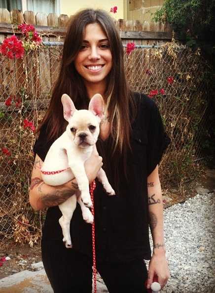 Christina Perri standing in the garden while holding her white French Bulldog puppy
