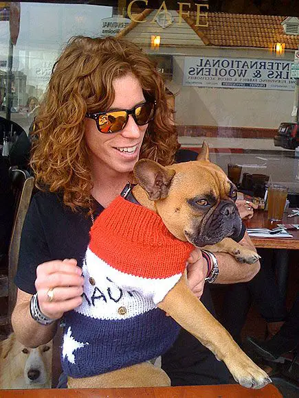 Shaun White sitting on the chair with his French Bulldog wearing a sweater sitting on his lap