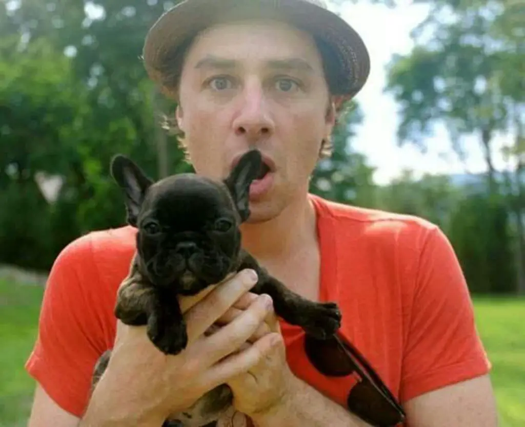 Zach Braff with his shock face holding his black French Bulldog puppy