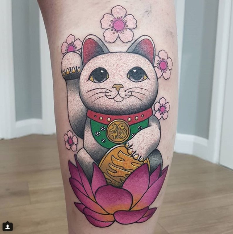 A japanese style Lucky Cat sitting in a pink flower tattoo on the leg