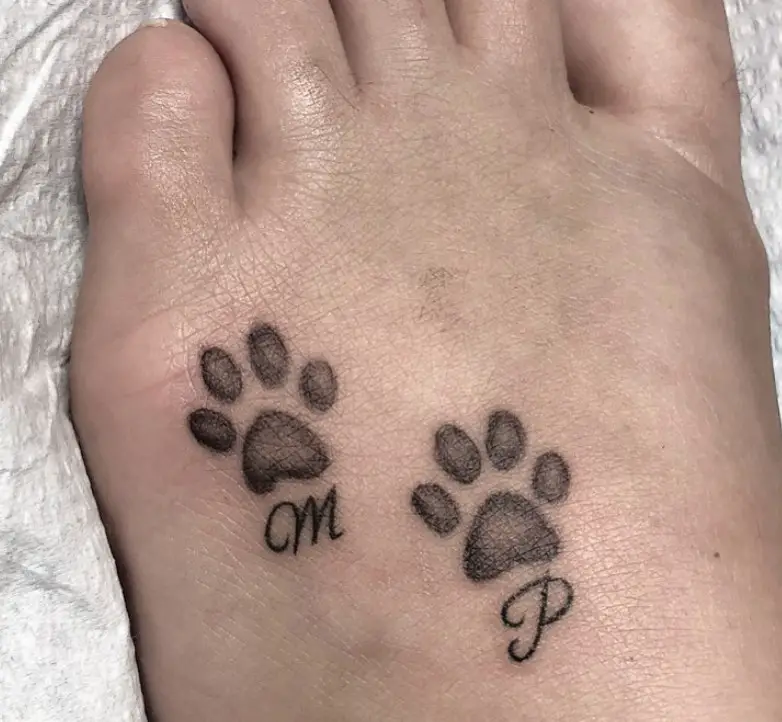 two black paw prints with initial tattoo on the feet