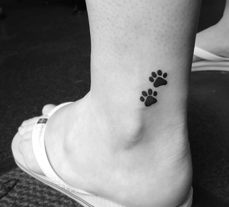 two small black paw print tattoo on the ankle