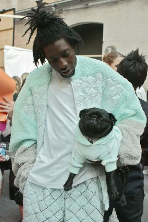 Coolio carrying his pug on his side wearing a matchy sweater