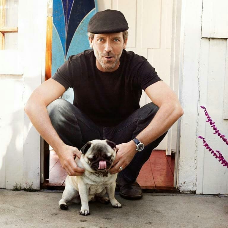 Hugh Laurie sitting by the door while petting his pug