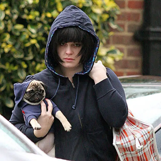 Kelly Osbourne walking in the street wearing a sweater while carrying his pug wearing a cute sweater