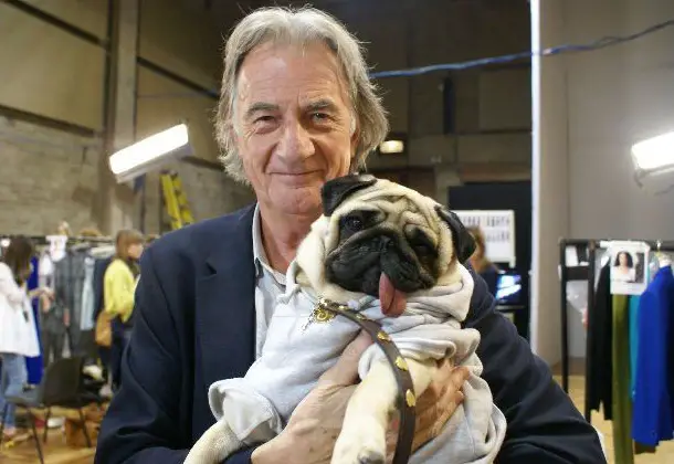 Paul Smith carrying his Pug wearing a sweater while its tongue is sticking out