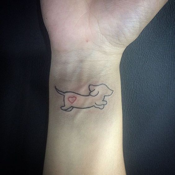 outline of a running dog with a red heart on its butt tattoo on the wrist