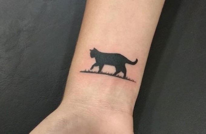 black cat walking on the grass tattoo on wrist