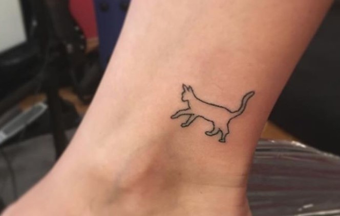 outline of a walking cat tattoo on the ankle