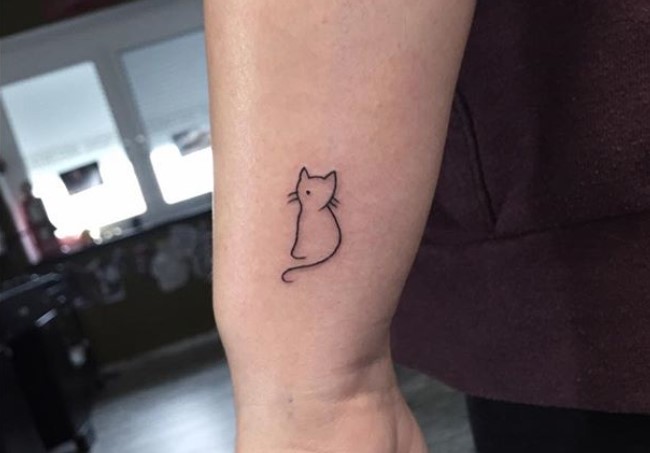 outline of a sitting cat tattoo on the side of the wrist