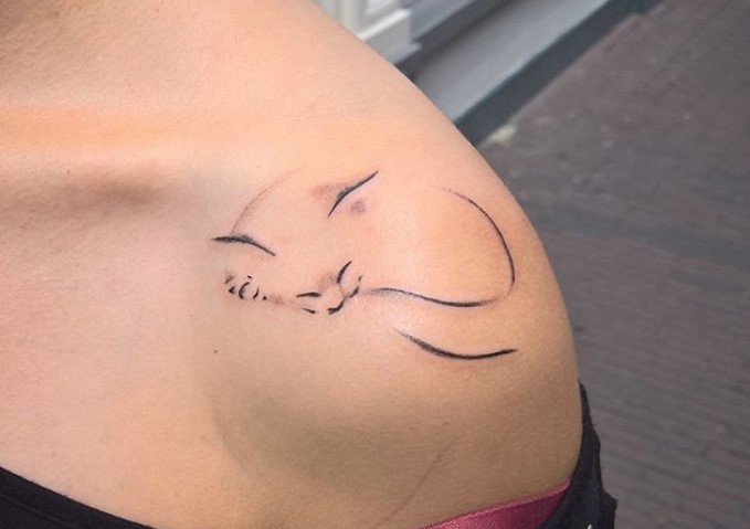 outline of a sleeping cat tattoo on the shoulder