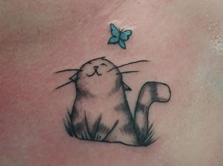 a cat sitting on the grass while looking at the blue butterfly on top of her tattoo