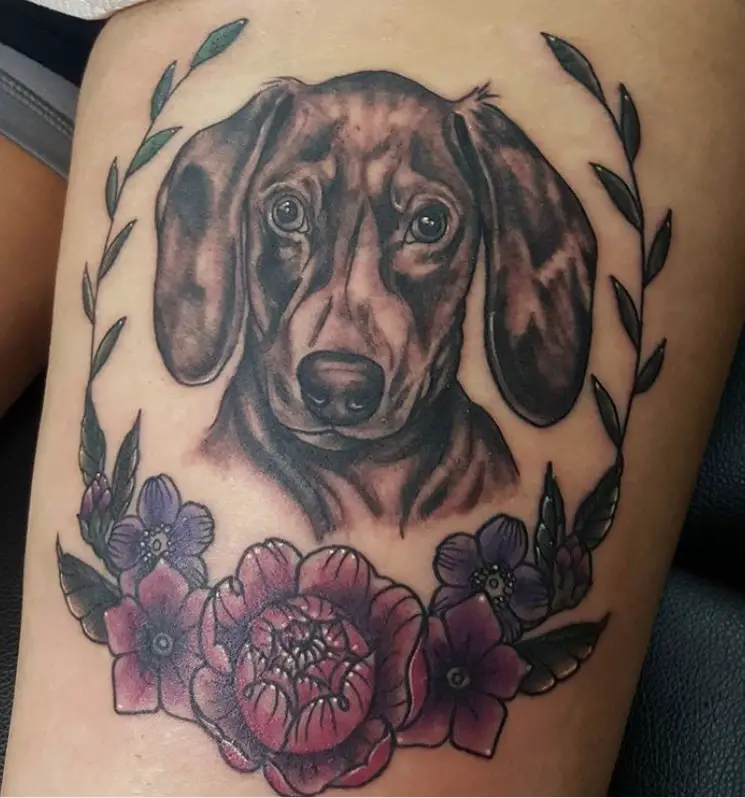 black and gray face of a Wiener Dog framed in a flowers and leaves tattoo on thighs
