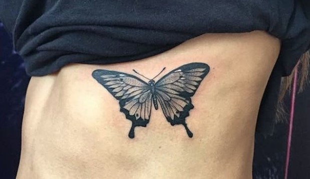 Black butterfly tattoo on the side of the body.