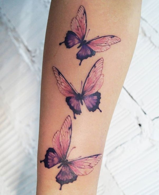 Three purple and pink butterfly tattoos on forearm.