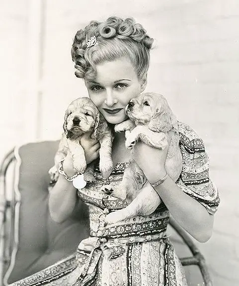 black and white photo of Joan Bennett holding her two Cocker Spaniel puppies close to her cheeks
