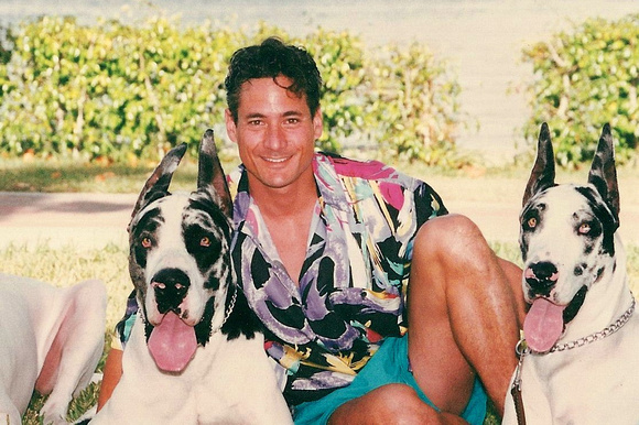 Greg Louganis sitting in the yard win between his two Great Danes