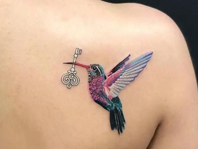 colorful hummingbird carrying a key with its beak tattooed on shoulder
