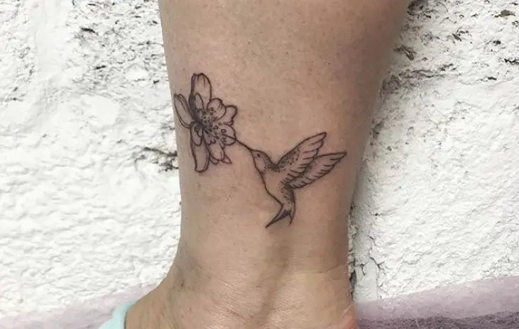 cute hummingbird feeding from a flower tattoo on ankle