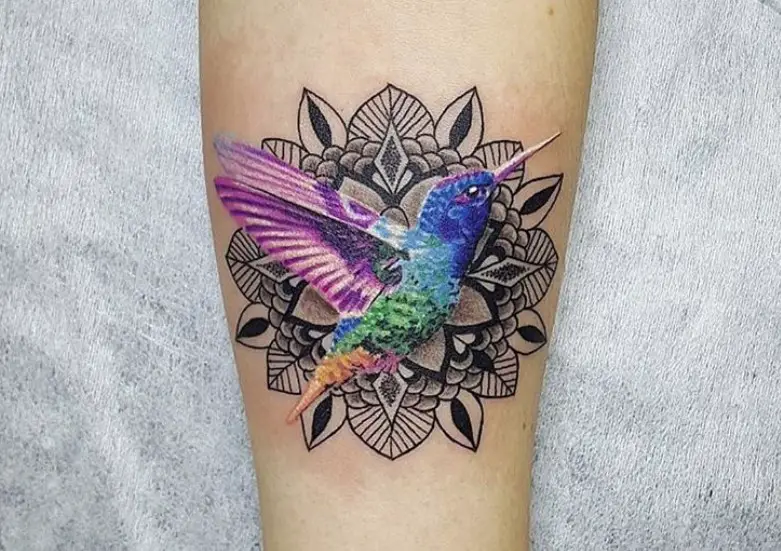 vibrant colored hummingbird tattoo with a flower pattern background in arms